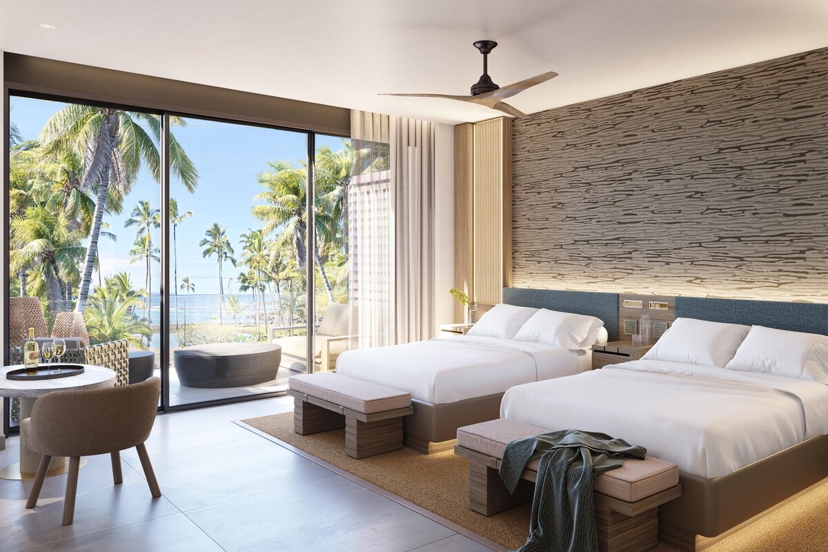 A modern hotel room with two beds, a seating area with a view of the ocean, and a large window.