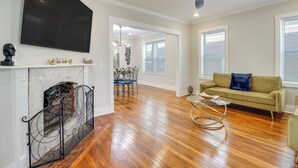 A spacious living room with hardwood flooring, a fireplace, a sofa, and a television mounted on the wall.