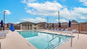 A pool area with lounge chairs, umbrellas, and a clear sky.