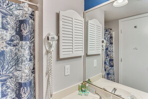 Une salle de bain avec un lavabo blanc, un miroir, un porte-serviettes et un rideau de douche à motifs bleus et blancs.