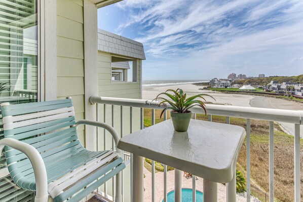 Un balcon donnant sur la plage, une petite table avec une plante et une chaise bleue.
