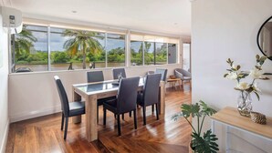Un espace repas comprenant une grande table et des chaises, une vue sur la verdure grâce à de grandes fenêtres et un plancher en bois.