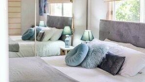 Une chambre à coucher avec un lit, des oreillers, une table de chevet, une lampe et une fenêtre.