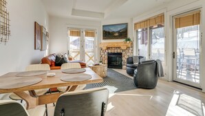 Ein geräumiges Wohnzimmer mit Kamin, großen Fenstern und einem Essbereich mit Holztisch und -stühlen.