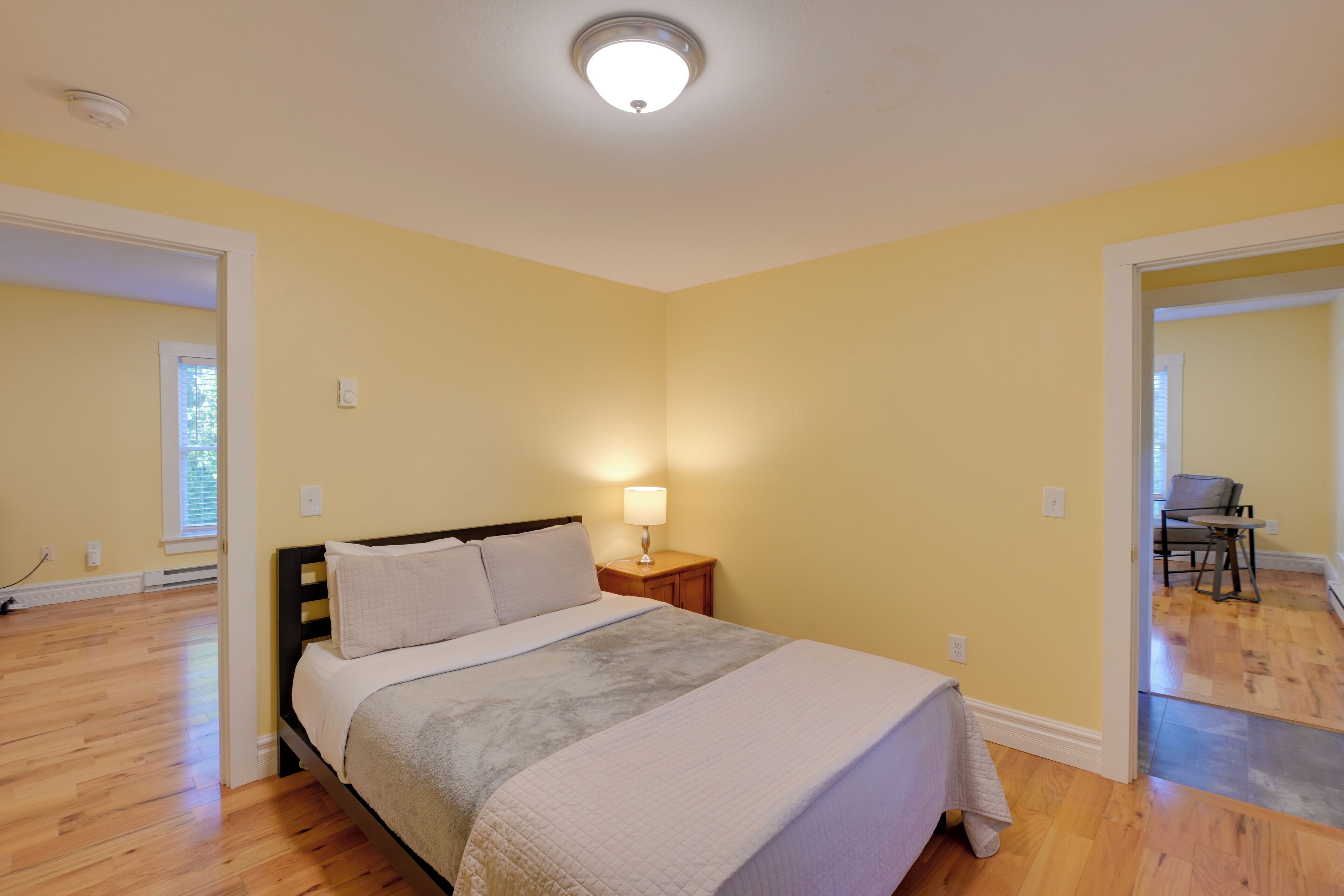 A bedroom with a bed, bedside lamp, and a view of another room.