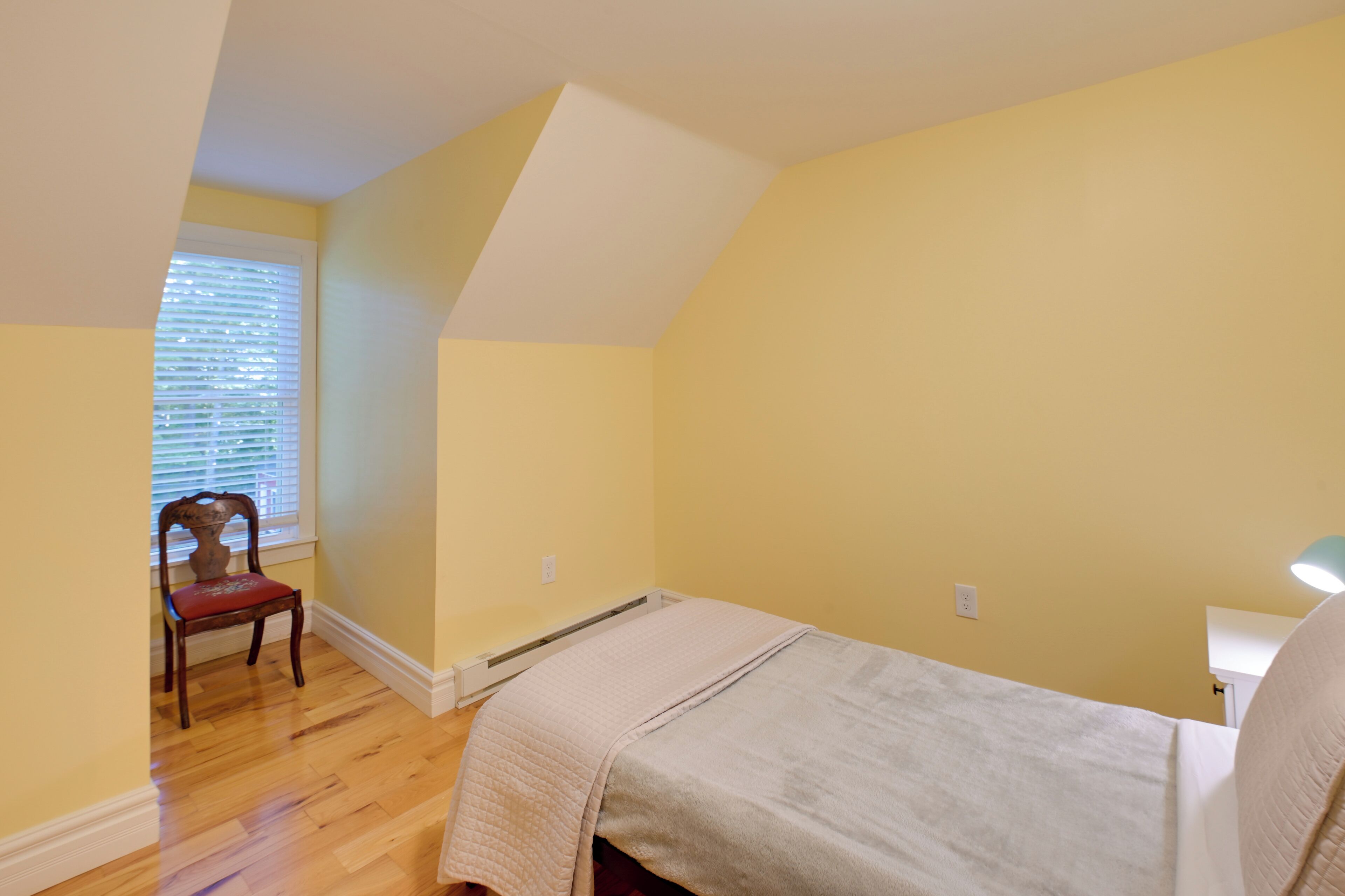 A bedroom with a bed, a chair, a window with blinds, and a radiator.