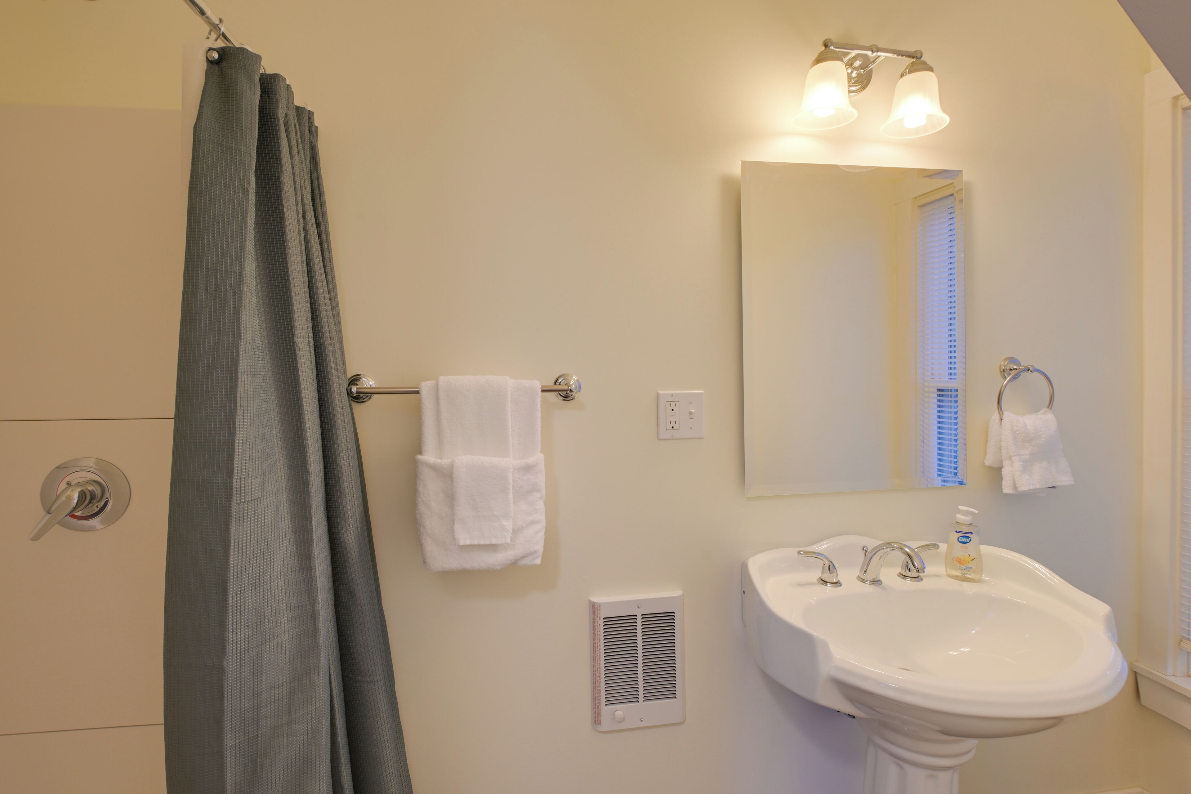 Un baño con cortina de ducha, un lavabo, un espejo y dos toallas colgadas de ganchos.