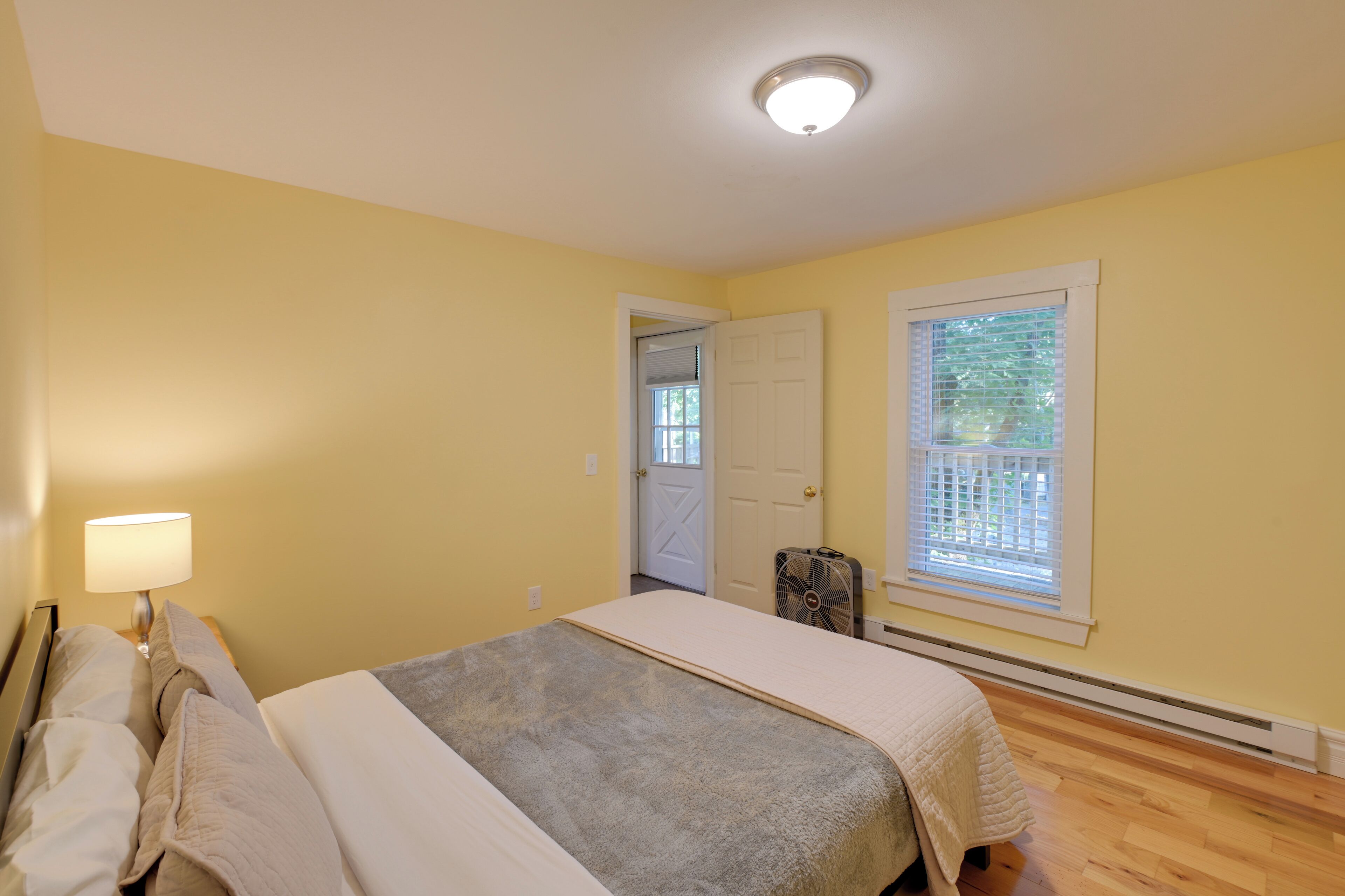 A bedroom with a bed, bedside lamp, and a window with blinds.