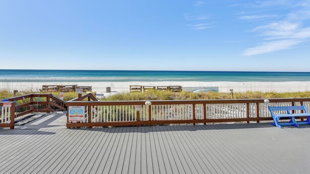 Une promenade en bois menant à une plage, avec un banc bleu et des tables de pique-nique.