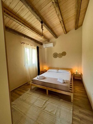 Et soveværelse med en træseng, ventilator, klimaanlæg og et vindue med gardiner.
