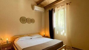 Een bed met houten frame in een kamer met schuine wand, een wandairconditioner en een raam met gordijnen.