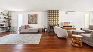 Un salón amplio con suelo de madera, chimenea, televisor y estantería.