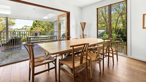 Un comedor amplio con una mesa y sillas de madera, ventanas grandes que ofrecen vistas al exterior y un puerta corrediza de vidrio que da a una terraza.