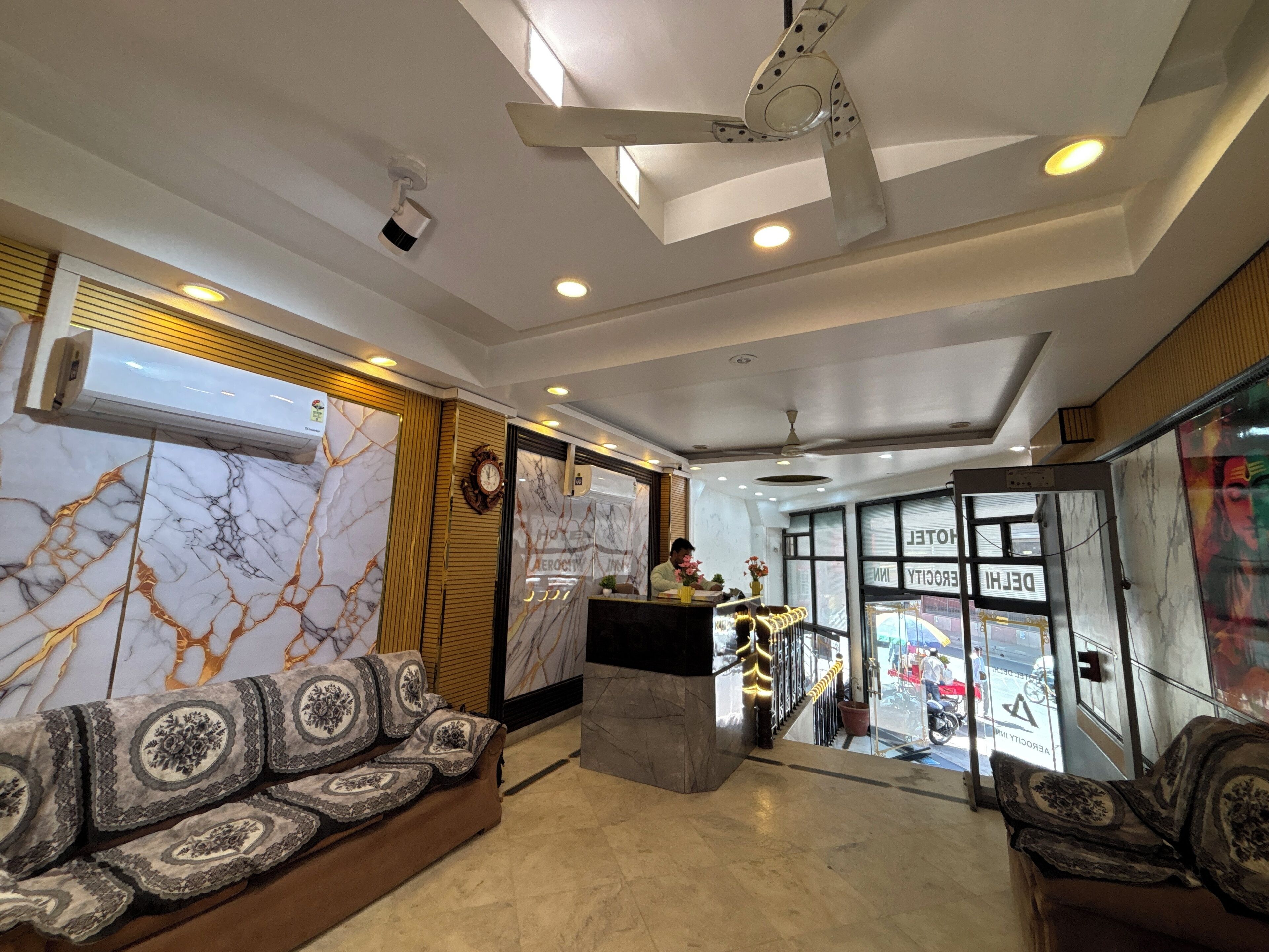 A hotel lobby with marble walls, a reception desk, seating area, and a view of the street through large windows.
