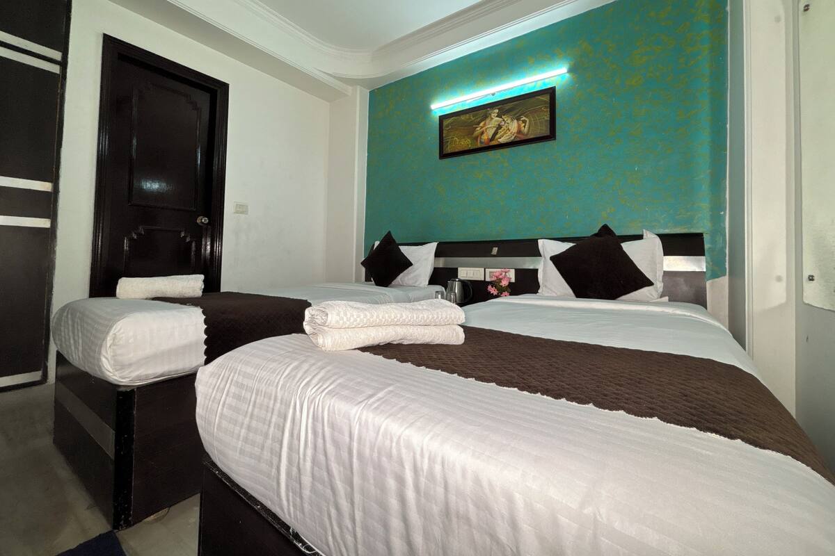A hotel room with two beds, a dark wooden wardrobe, a teal accent wall, and a framed artwork above the beds.