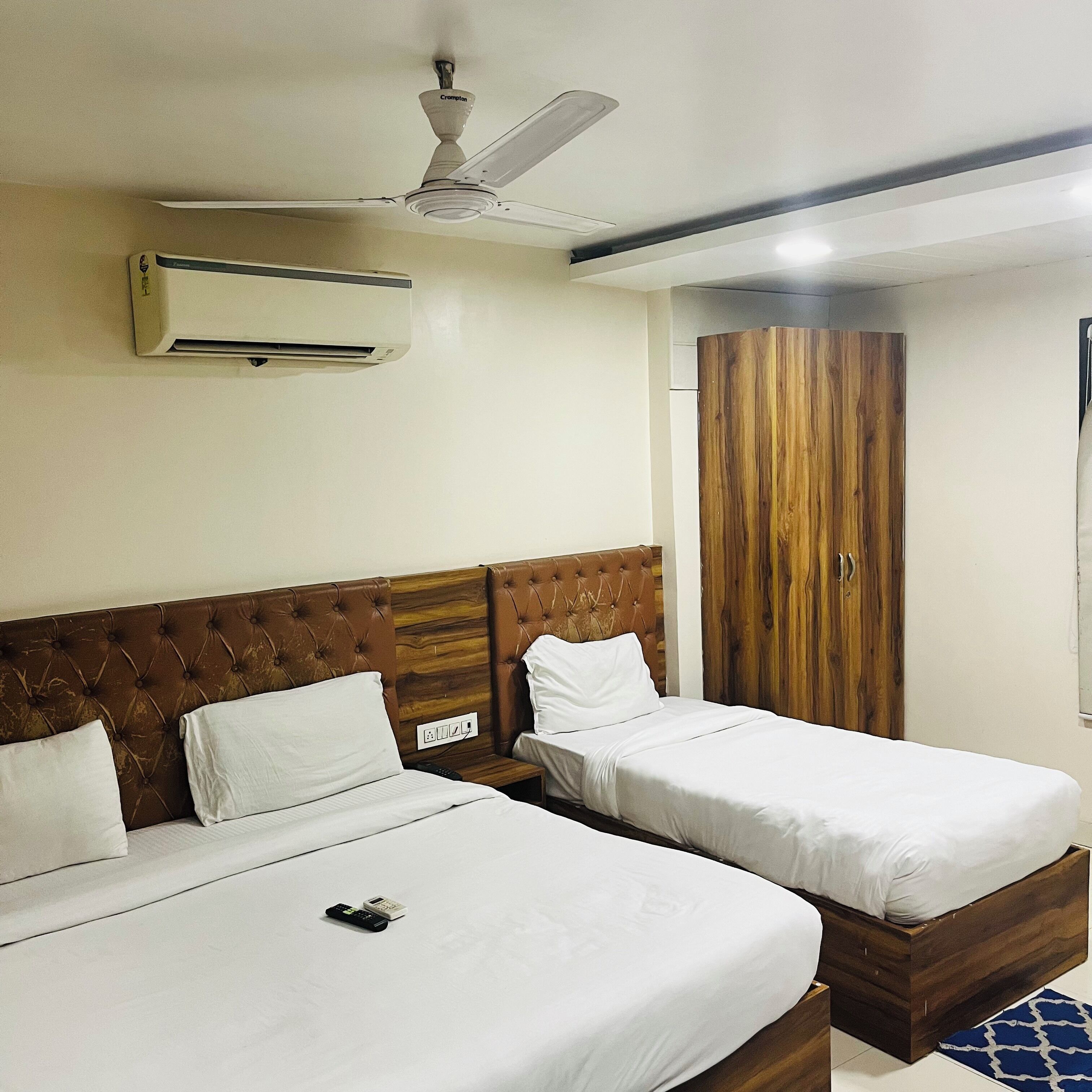 A hotel room with two beds, a ceiling fan, an air conditioning unit, and a wardrobe.