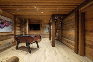 A wooden-floored room with a foosball table, wooden walls, and a staircase leading to another level.