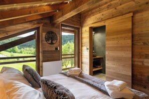 A wooden cabin bedroom with a bed, towels, and a view of the outdoors. - ✨ Chalet Marcel – Luxury Chalet with Hot Tub, Sauna & Forest Setting (Gérardmer)