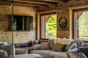 A cozy cabin interior with a sofa, a mounted television, and large windows. - ✨ Chalet Marcel – Luxury Chalet with Hot Tub, Sauna & Forest Setting (Gérardmer)