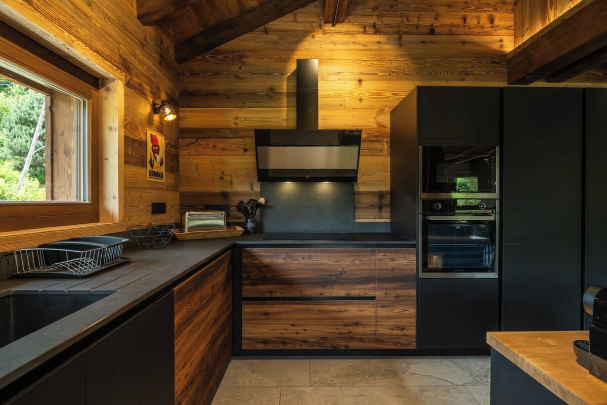 Cocina moderna con paredes de madera, horno empotrado y ventana que proporciona luz natural.