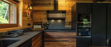 Cocina moderna con paredes de madera, horno empotrado y ventana que proporciona luz natural.
