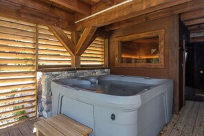 A wooden cabin with a hot tub, stone walls, and a wooden deck.