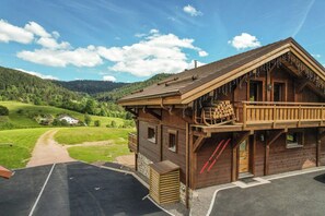 A wooden chalet with a balcony, a ski slope, and a view of a green valley. - ✨ Chalet Marcel – Luxury Chalet with Hot Tub, Sauna & Forest Setting (Gérardmer)