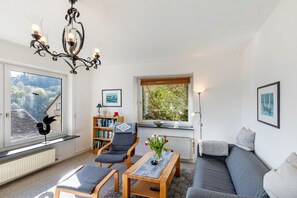 Un salon comprenant un canapé, des fauteuils, une table basse, un lustre, une bibliothèque et une fenêtre donnant sur un beau paysage.
