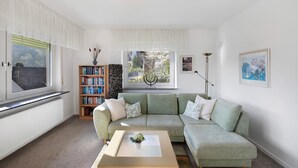 A living room with a green sofa, a coffee table, a bookshelf, and a window with curtains. - Holiday Apartment 'Rheinblick' with Balcony and Wi-Fi (Sankt Goar)