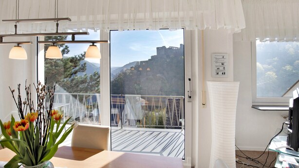 A room with a balcony, a dining table, and a view of a mountainous landscape. - Holiday Apartment 'Rheinblick' with Balcony and Wi-Fi (Sankt Goar)