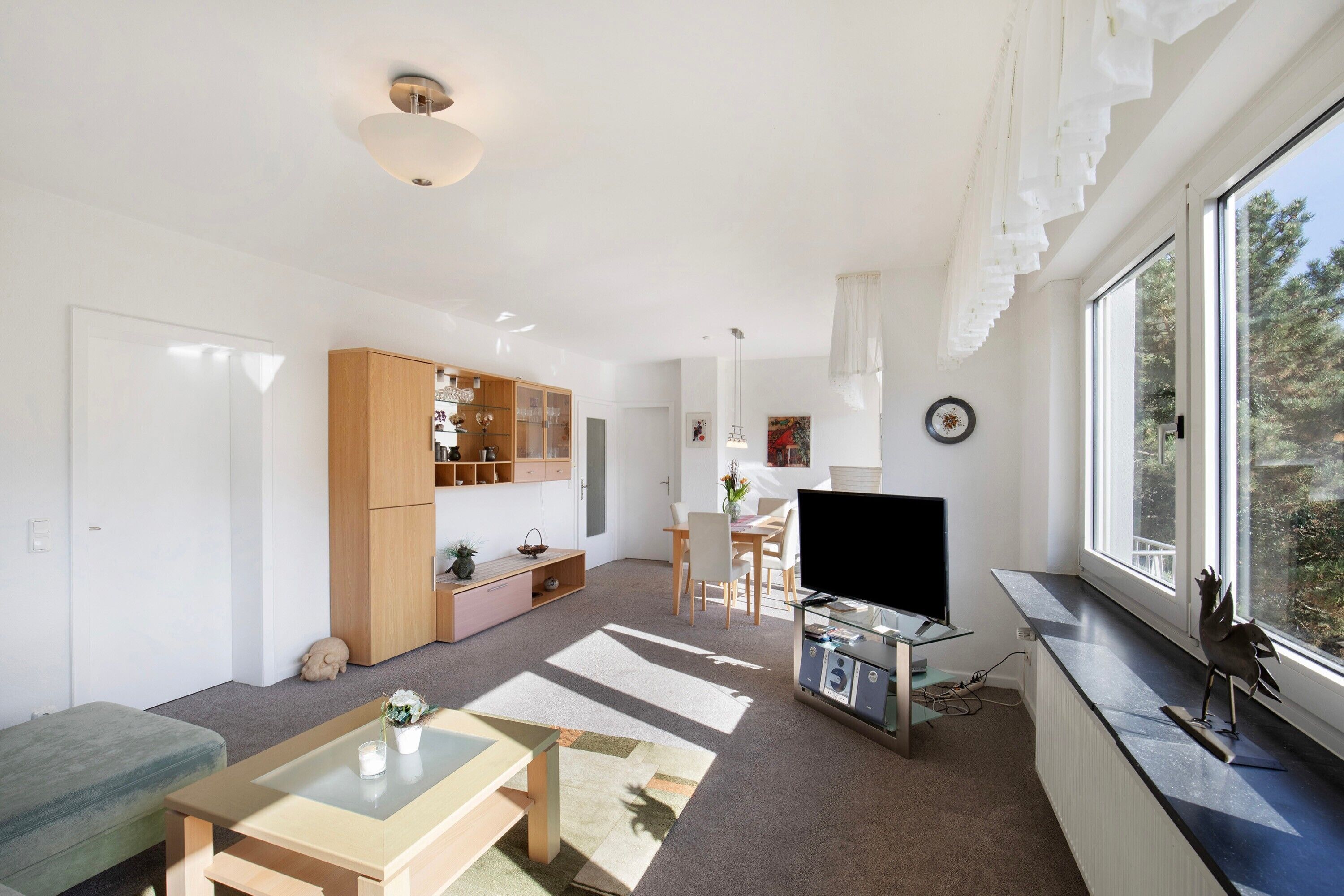 Een moderne woonkamer met een televisie, zitmeubels, een eethoek en een groot raam.
