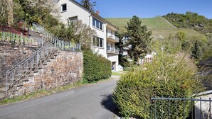 A residential street with a two-story house, a staircase, and a hillside in the background. - Holiday Apartment 'Rheinblick' with Balcony and Wi-Fi (Sankt Goar)