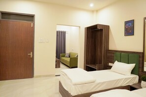 A hotel room with a wooden door, a green sofa, a bed with a green headboard, and a framed picture on the wall.