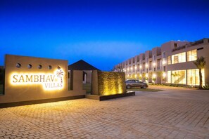 A modern hotel entrance with a sign reading "Sambhav Villas" and a paved driveway leading to the building. - SAMBHAV VILLAS (Pushkar)