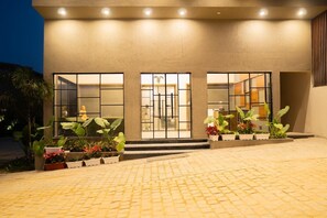 A modern building with a paved entrance area, large windows, and potted plants.