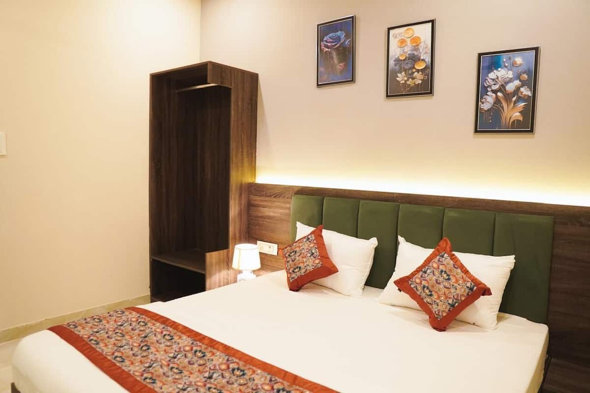 A hotel room with a large bed, green upholstered headboard, and a wooden wardrobe.