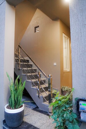 Una escalera con barandilla, una planta en maceta y una lámpara fijada a la pared.
