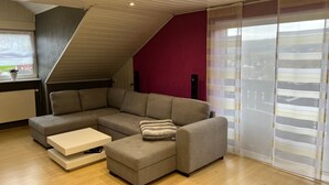 Un salon moderne avec un canapé d’angle, une petite table blanche et un escalier menant à un niveau supérieur.