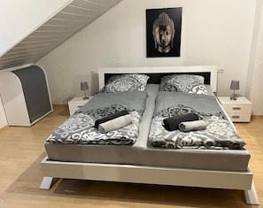 A double bed with patterned bedding, two bedside tables with lamps, a wall-mounted Buddha statue, and a sloped ceiling. - Apartment 'Ausblick' with Balcony and Wi-Fi (Hausen)