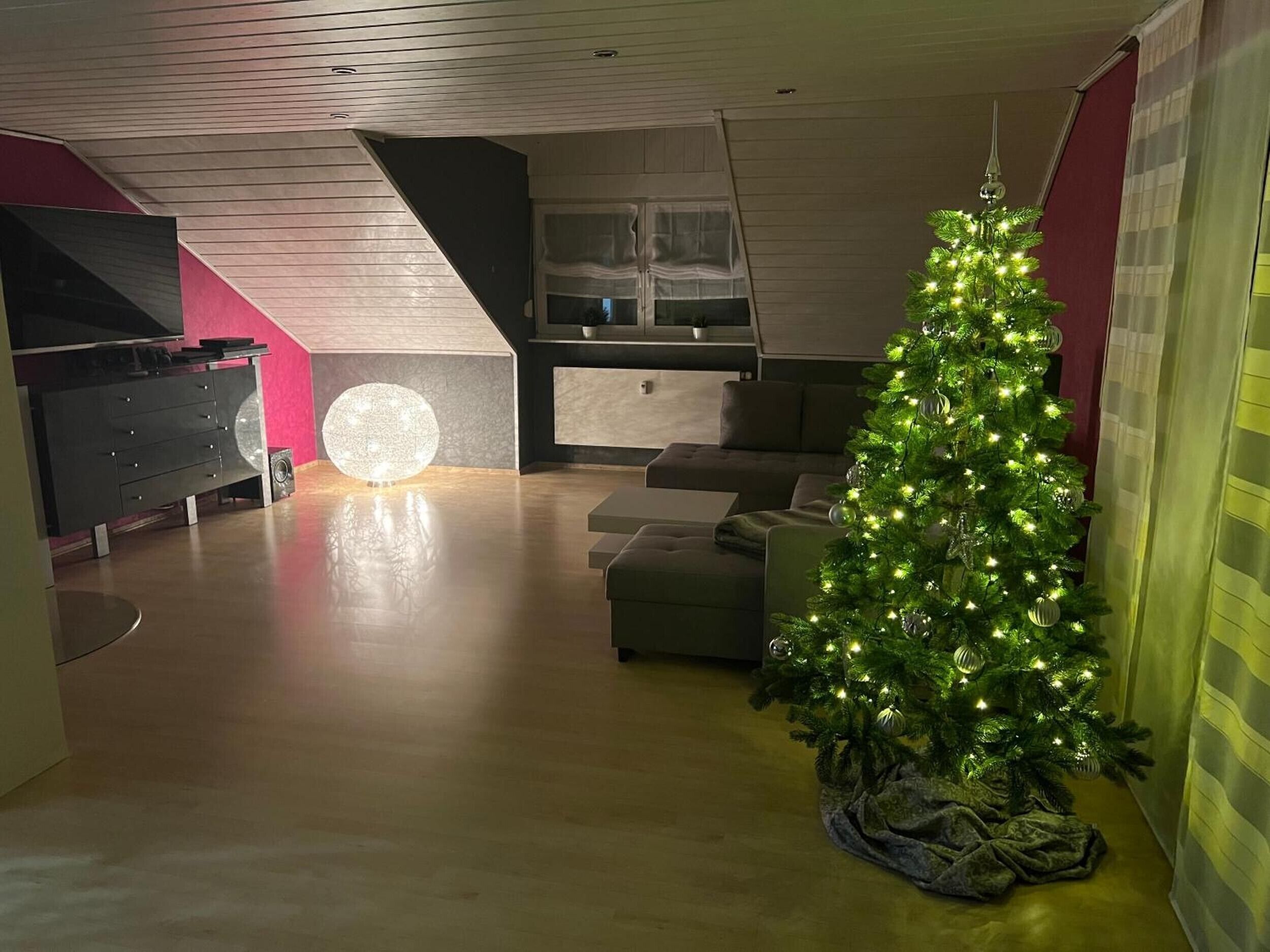 A modern living room with a Christmas tree, a large spherical light, and a television.