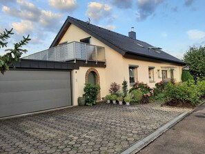Une maison à deux étages avec une porte de garage grise, une arche en briques et un balcon doté de rampes en métal.