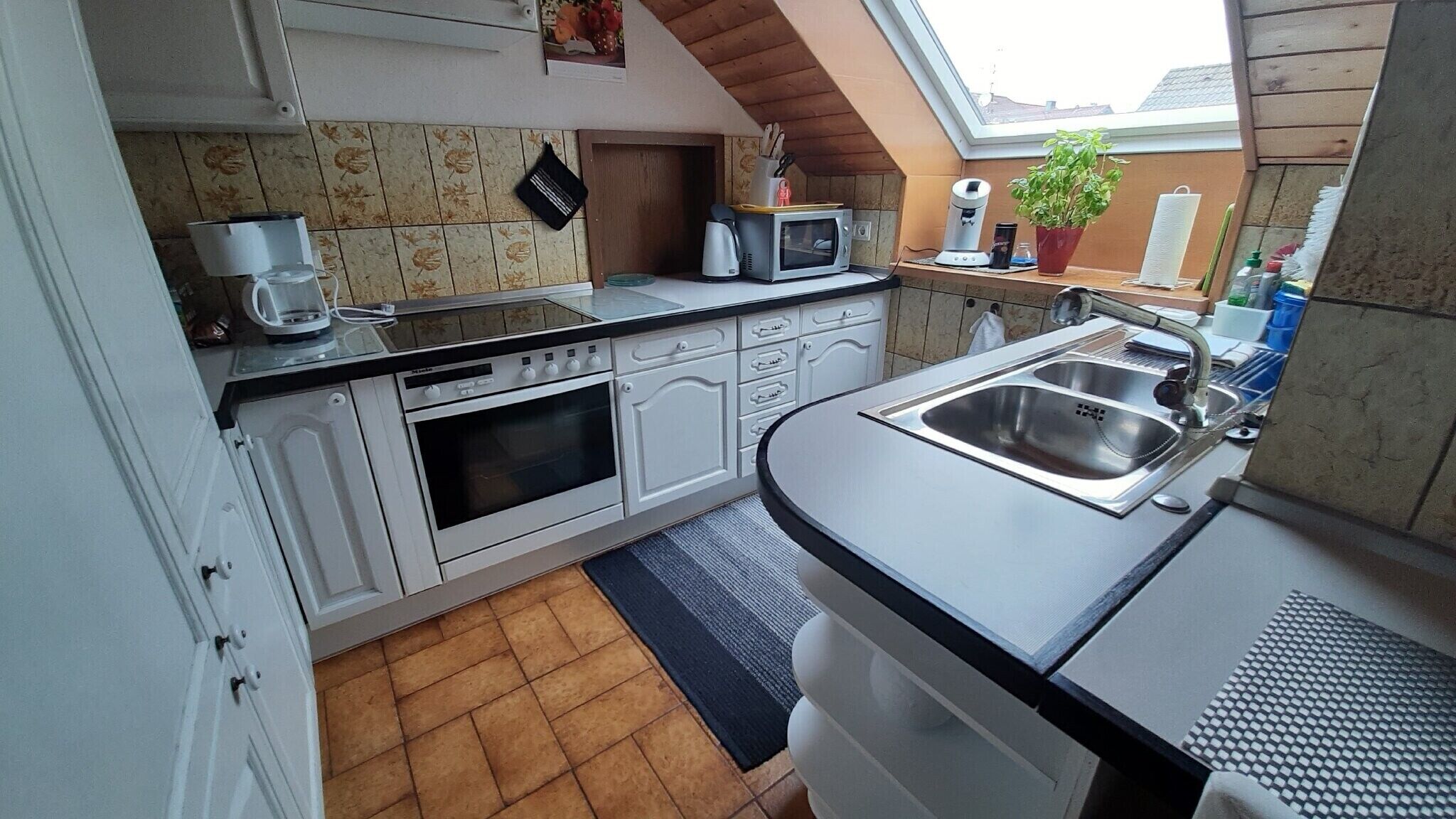 A compact kitchen with a microwave, oven, and sink, a small window, and a potted plant.