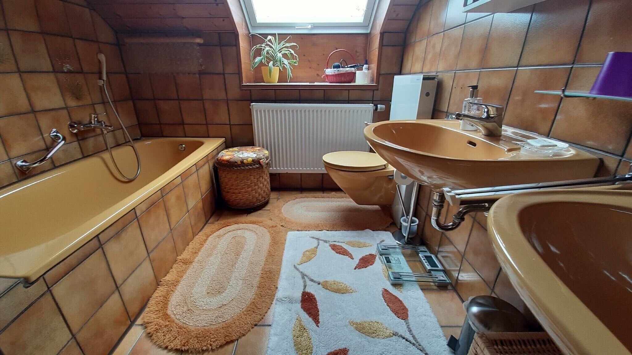 A compact bathroom with a bathtub, toilet, and sink, featuring wooden walls and a skylight.