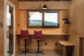A wooden interior with two bar stools, a window with a view, and a pendant light.