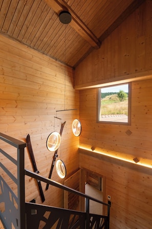 Een houten interieur met een trap, een raam met uitzicht en hanglampen.