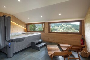 A modern bathroom with a hot tub, wooden benches, and large windows offering a view of a hilly landscape. - Chalet Nanook - 10 pers - Spa - Sauna (Xonrupt-Longemer)