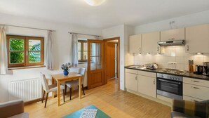 Une cuisine moderne avec un coin repas, un plancher en bois et une vue sur l’extérieur grâce à la porte ouverte.