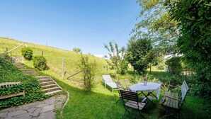 Un jardin avec un chemin en pierre, une table entourée de chaises et une petite table sur laquelle est posé un vase.