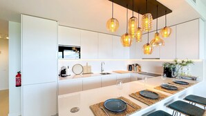 Una cocina moderna con armarios blancos, una isla central con taburetes y luminarias colgantes.