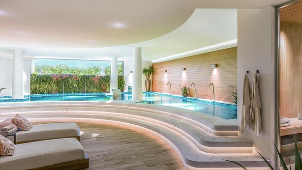 Un área de piscina interior moderna con una zona de estar curva, una pared de madera y vistas a zonas verdes al exterior.